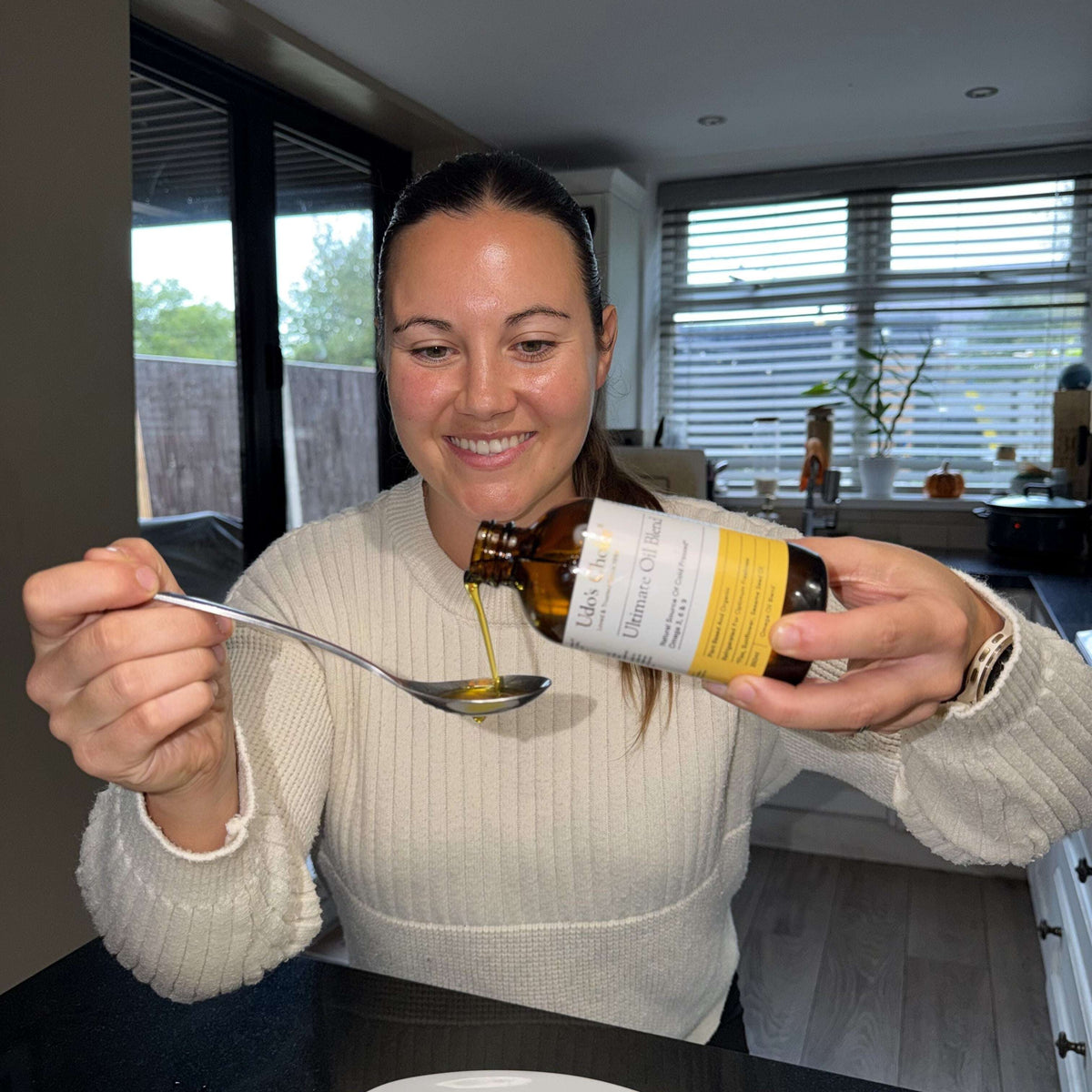 Woman in the kitchen pouring Ultimate Oil Blend Vegan Omega 369 onto a tablespoon